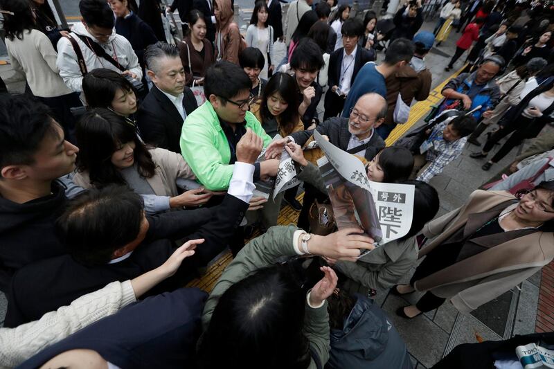 A Yomiuri newspaper worker hands a copy of the extra edition reporting the enthronement ceremony for the 59-year-old Emperor Naruhito.  AP