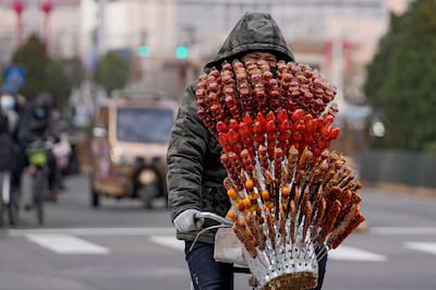 A vendor with a variety of sugar-coated Chinese haw crosses an intersection in Beijing, on January 26. AP