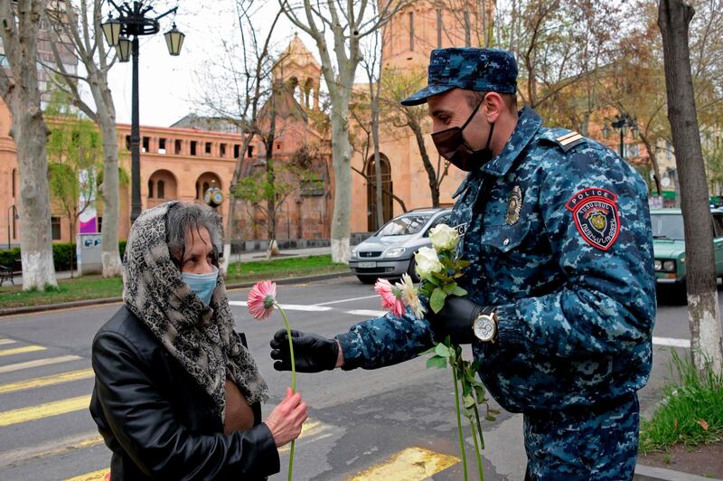 A police officer wearing a face mask and gloves presents a flower to a woman on the Motherhood and Beauty Day in Yerevan, Armenia.  AFP