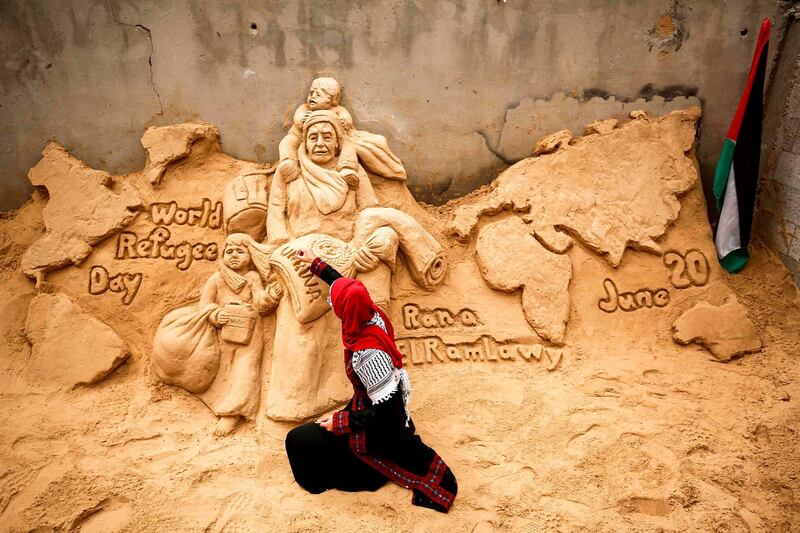 TOPSHOT - Palestinian sand sculptor Rana Ramlawi finishes a new artwork creation commemorating World Refugee Day, a day dedicated by the United Nations General Assembly to raising awareness of the situation of refugees throughout the world, in Gaza City on June 20, 2020, depicting a woman carrying a child and a sack of flour bearing the logo of the United Nations Relief and Works Agency for Palestine Refugees (UNRWA) with a child behind holding a jerry can of water, all standing before a map of the world. Some five million individuals are refugees registered with the UNRWA, of whom more than 1.5 million (nearly one-third) live in 58 recognised refugee camps in the Gaza Strip and the West Bank including East Jerusalem, in addition to Jordan, Lebanon, and Syria. Palestine refugees are defined by the UNRWA as "persons whose normal place of residence was Palestine during the period 1 June 1946 to 15 May 1948, and who lost both home and means of livelihood as a result of the 1948 conflict." / AFP / MOHAMMED ABED
