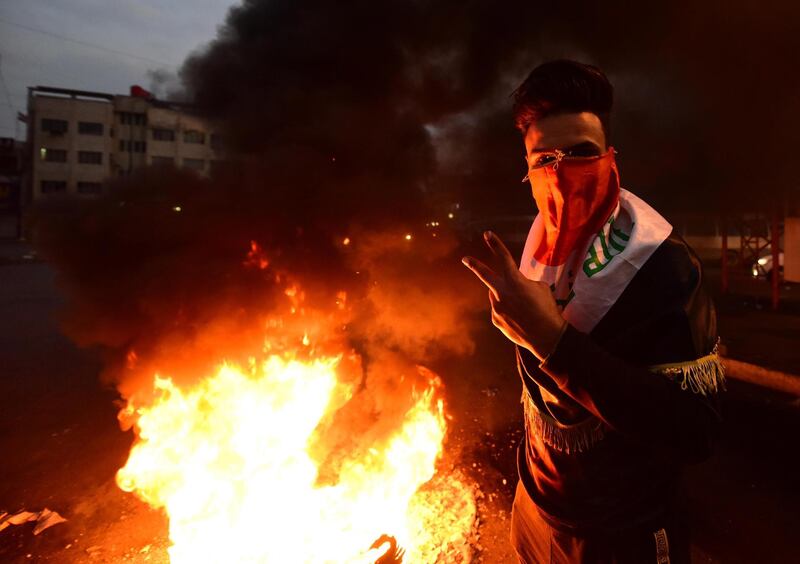 An Iraqi protester flashes the victory sign as he stands next to burning tyres set ablaze to block a street during a strike and anti-government demonstrations at the Al-Tayaran Square in central Baghdad.  EPA