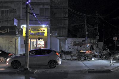 A fruit seller with his horse and cart stands next to the Gelato di Gaza shop, as traffic passes by. Location: Al-Nasser Street, Gaza City. 4 February 2020. Rosie Scammell  for The National