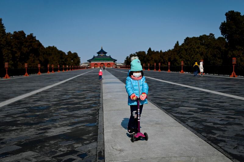 A girl wearing a face mask plays on her scooter at a park in Beijing.  AFP