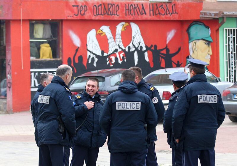 Police officers stand by the graffiti that shows Serbian coat of arms and silhouettes of people, reading: "... because there's no turning back", in northern Serb-dominated part of ethnically divided town of Mitrovica, Kosovo, Friday, Nov. 23, 2018. Kosovo police arrested three ethnic Serbs, including two police officers, early Friday on suspicion of involvement in the killing of a leading Serb politician in the north of the country. (AP Photo/Bojan Slavkovic)