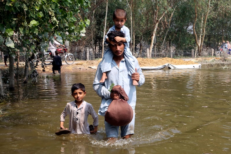 A man and his children wade through floodwaters in Charsadda, Pakistan. AP