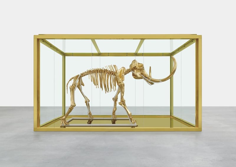 British artist Damien Hirst’s latest piece entitled Gone but Not Forgotten, which features the gilded skeleton of a woolly mammoth in a steel and glass vitrine, is displayed. Famed British artist Damien Hirst has created a gilded woolly mammoth skeleton encased in a gold tank to be auctioned off at the annual amfAR Cinema Against Aids gala in Cap d’Antibes, southern France, on May 22, 2014. Prudence Cuming Associates via Damien Hirst / AP photo