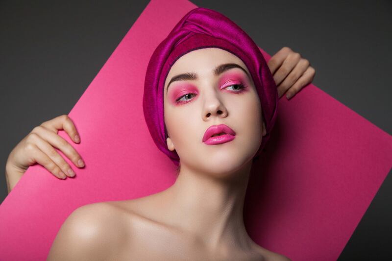 Sensual model wearing pink turban and pink makeup standing against crop hands holding pink paper. Getty Images