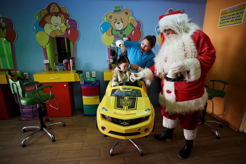 The owner of a kids hair salon, dressed as Santa Claus, offers candies to a child while a hairstylist cuts her hair in Monterrey, Mexico. Reuters