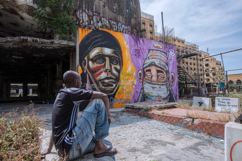A Sudanese man smokes a cigarette as he sits looking at a graffiti depicting an African man and a white woman with a mask, in Beirut, Lebanon.  EPA