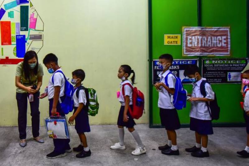 A teacher administers hand sanitizer to pupils. AFP