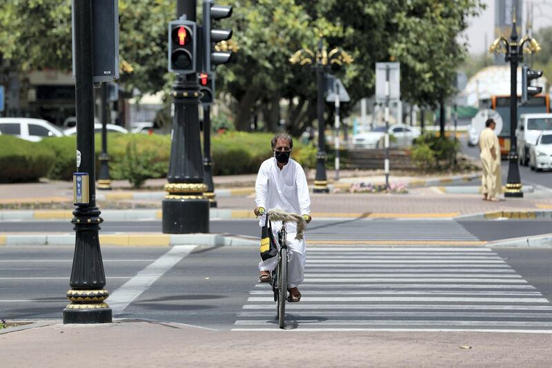 Al Ain, United Arab Emirates - Reporter: N/A: A man wearing a facemask rides his bike across the street in Al Ain. Thursday, April 9th, 2020. Al Ain. Chris Whiteoak / The National