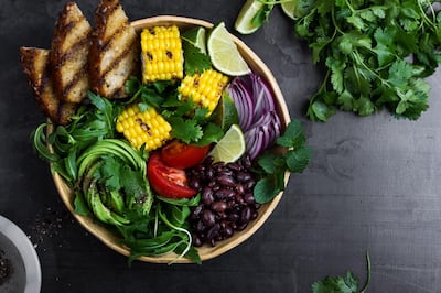 Colorful healthy vegan meal. Salad bowl with abocado rose, grilled corn, tomatoes, black beans, whole grain toasted bread, arugula, red onion and cilantro. Getty Images