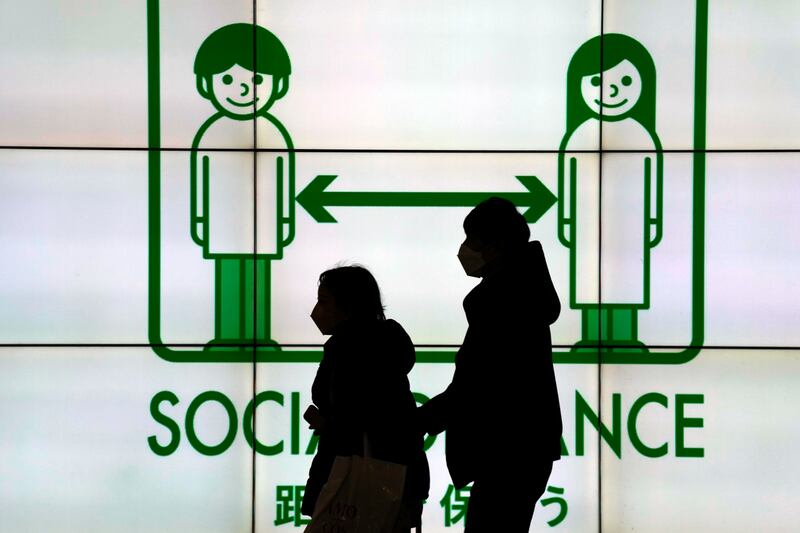 People wearing face masks are silhouetted against a public awareness notice about social distancing in the Japanese capital Tokyo. AP