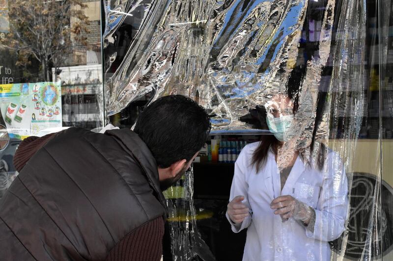 A pharmacist, wearing a face mask and gloves as a preventive measure against Covid-19, talks to a customer from behind a nylon curtain put up at the front of the pharmacy in Damascus, Syria.  EPA