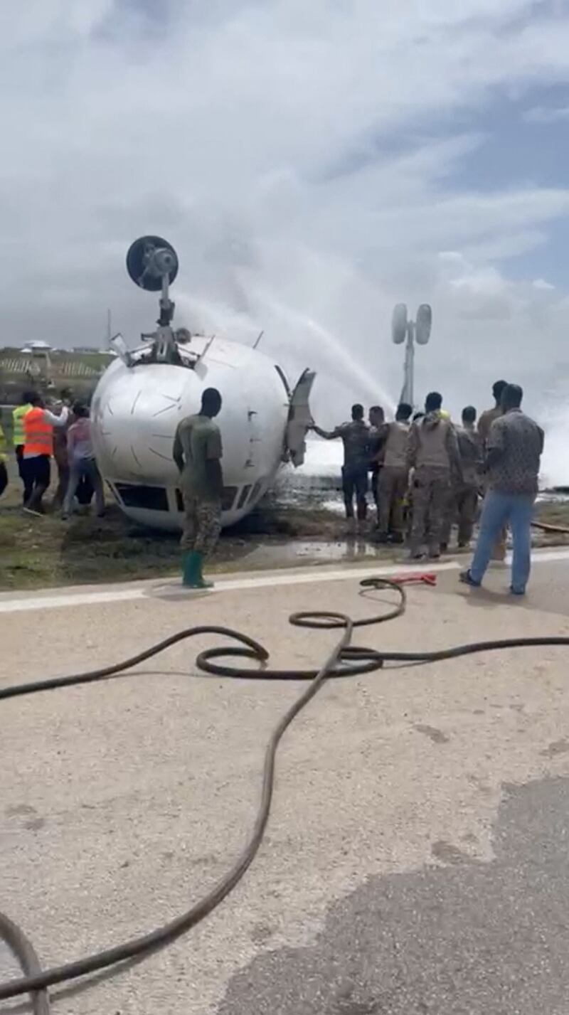 Firefighters spray water on a plane that flipped over after a crash landing, in Mogadishu, Somalia, July 18, 2022, in this screen grab obtained from a social media video obtained by Reuters.   THIS IMAGE HAS BEEN SUPPLIED BY A THIRD PARTY NO RESALES.  NO ARCHIVES