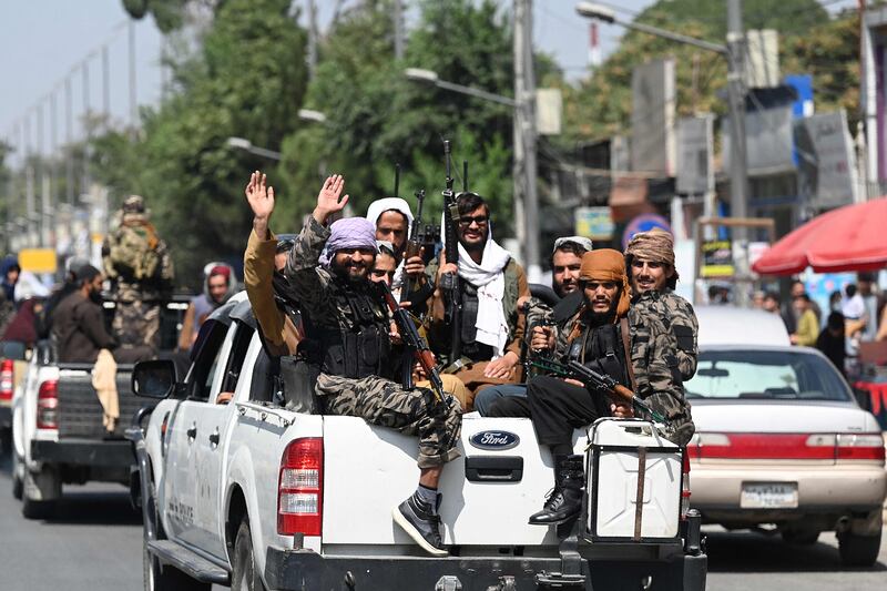 Taliban fighters wave as they patrol in a convoy along a street in Kabul. AFP
