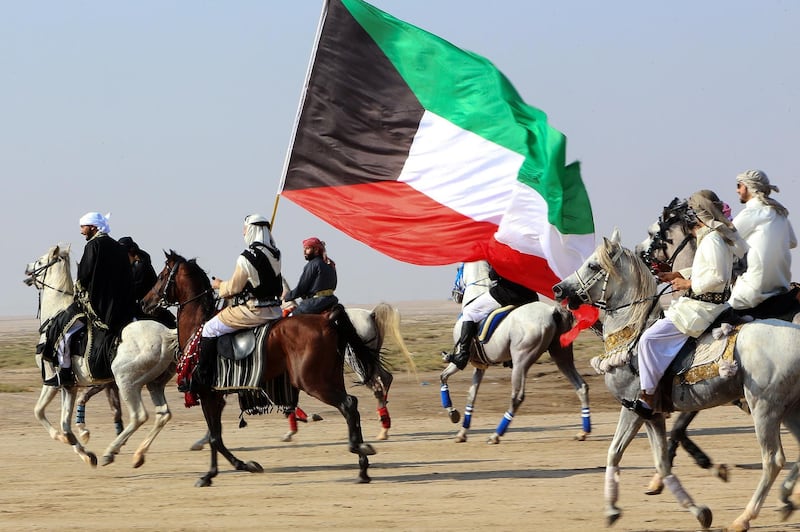 Members of the Kuwaiti knights team carry a national flag as they perform with their horses on the sea side, 70 kms west of the capital Kuwait City on December 11, 2020. / AFP / YASSER AL-ZAYYAT
