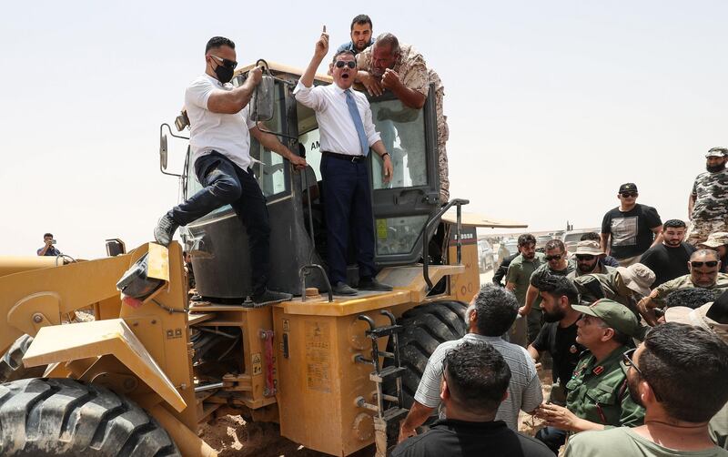 Libyan Interim Prime Minister Abdulhamid Dbeibah, waves as he stands atop an excavator on June 20, 2021, in the town of Buwairat al-Hassoun, during a ceremony to mark the reopening of 300-kilometre road between the cities of Misrata and Sirte,  Libya's unity government today reopened the coastal highway linking the country's east and west, that was cut off in 2019 as eastern-based military strongman Khalifa Haftar launched an offensive to seize the capital Tripoli. 
It connects the war-torn North African country's border with Tunisia to its frontier with Egypt. / AFP / Mahmud TURKIA

