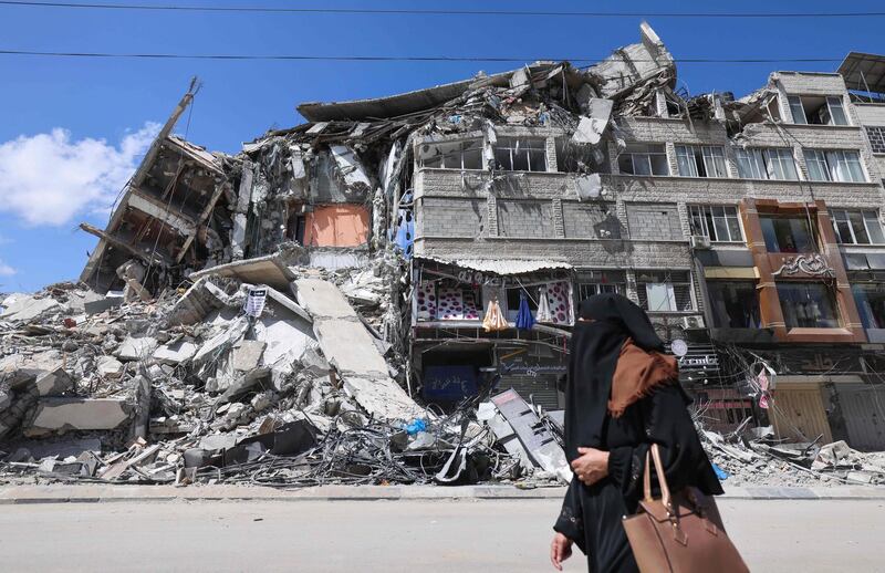 TOPSHOT - A Palestinian woman walks past a dsetroyed building in the al-Rimal commercial district in Gaza City on May 22, 2021, following a ceasefire between Israel and Palestinian militants in the Israeli-blockaded enclave. As the ceasefire holds, humanitarian aid began to enter the enclave ravaged by 11 days of bloodshed. While thousands of displaced Palestinians returned to their homes, and Israelis began to resume normal life a day earlier, international focus turned to the reconstruction of the bomb-shattered Gaza Strip. / AFP / Emmanuel DUNAND
