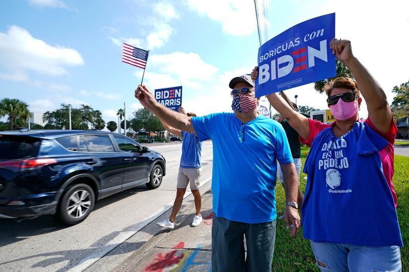 Dennis Marshall, front left, and his Puerto Rican wife, Nettie Marshall, wave flags and signs to passing motorists during a rally supporting Democratic presidential candidate Joe Biden in Orlando, Florida. AP Photo