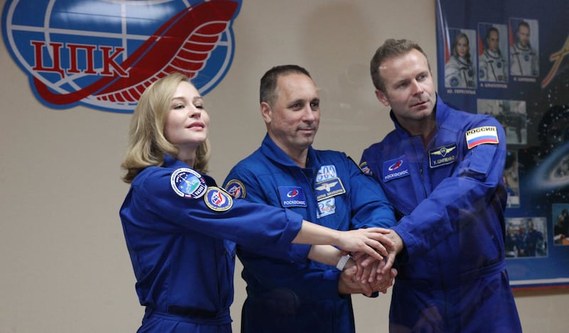 This handout photo taken and released on October 4, 2021 by the Russian Space Agency Roscosmos shows crew members, cosmonaut Anton Shkaplerov (C), actress Yulia Peresild (L) and film director Klim Shipenko, shaking hands behind a glass wall during a news conference ahead of the expedition to the International Space Station (ISS) at the Baikonur Cosmodrome, Kazakhstan.  - Roscosmos is dispatching the 36-year-old screen star Yulia Peresild along with director Klim Shipenko, 38, and cosmonaut Anton Shkaplerov in the race against time to beat a parallel Hollywood project led by actor Tom Cruise.  The launch to ISS is scheduled for October 5, 2021.  (Photo by Andrey SHELEPIN  /  GCTC / Russian space agency Roscosmos  /  AFP)  /  RESTRICTED TO EDITORIAL USE - MANDATORY CREDIT "AFP PHOTO  /  Russian space agency Roscosmos /  Andrey SHELEPIN" - NO MARKETING - NO ADVERTISING CAMPAIGNS - DISTRIBUTED AS A SERVICE TO CLIENTS