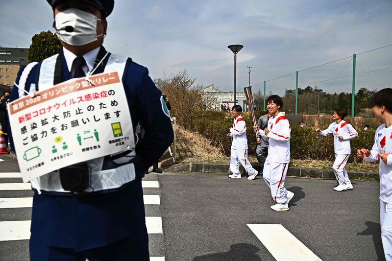 Azusa Iwashimizu, a member of Japan women's national football team, carries the Olympic flame as a guard holds a sign for Covid-19 precautions. AFP