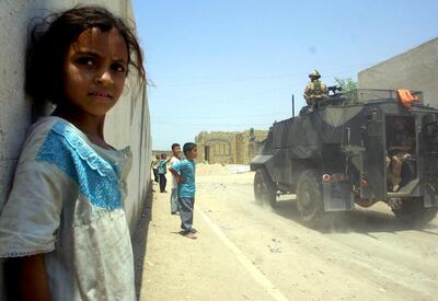 An Iraqi girl stands by as British soldiers patrol a street in the southern city of Basra 05 August 2003.  Most of Iraq has been plagued by a collapse of basic services including security following the war to oust Iraqi President Saddam Hussein.  AFP PHOTO/Ahmad AL-RUBAYE (Photo by AHMAD AL-RUBAYE / AFP)