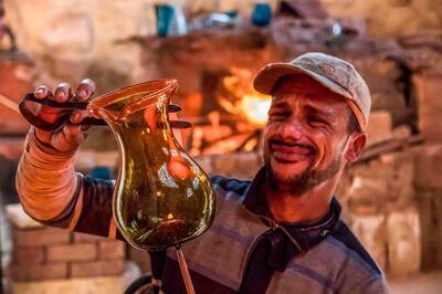 A glassblower sculpts a vessel at a workshop near the 15th century Sultan Qaitbay mosque complex in the "Desert of the Mamluks" (City of the Dead) area of Egypt's capital Cairo on November 1, 2020. In Egypt's "City of the Dead", centuries-old monuments are being restored and artisanal heritage revived, turning a corner of the vast historical cemetery into a vibrant neighbourhood full of life. Since 2014, a series of projects financed by the European Union has changed the face of this small section of the sprawling necropolis -- home to many people who are unable to afford Cairo's prohibitively high rents. / AFP / Khaled DESOUKI
