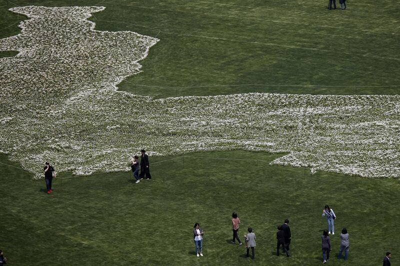 People walk around Seoul Square decorated with Marguerite in the shape of Korean Peninsula in Seoul.  Photo by Woohae Cho / Getty Images