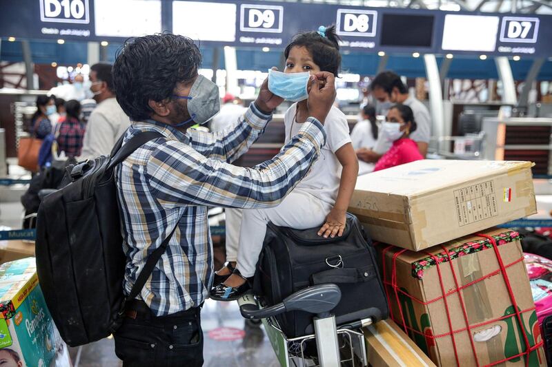 An Indian man puts on a mask on the face of a young girl as they wait with their luggage at the check-in counter for a repatriation flight from the Omani capital at Muscat International Airport.  AFP