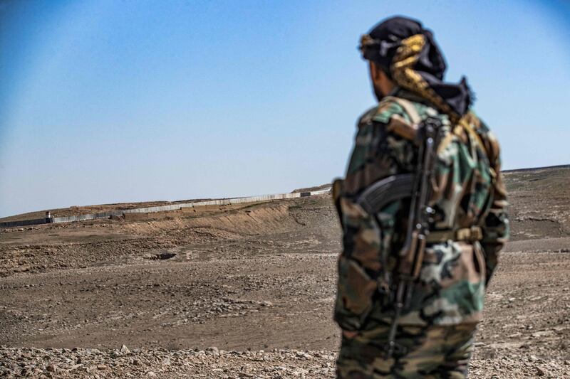 A Syrian Democratic Forces fighter near the town of Al Hol in Hasakah province watches construction work on a concrete border fence being erected on the Iraqi side of the border on March 29, 2022. AFP