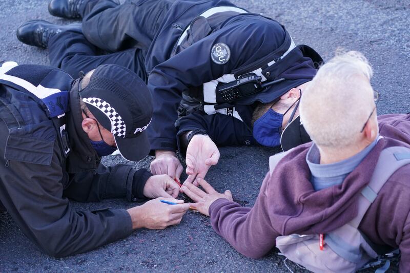 Police officers attempt to remove a protester glued to the road near to the South Mimms roundabout at the junction of the M25 and A1.