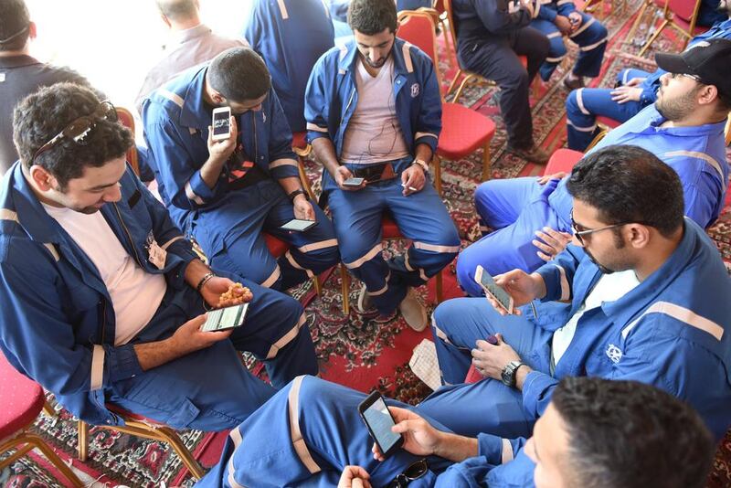 Kuwait Oil and Petrochemical Industries Union workers sit with their cellphones on the first day of an official strike over public sector pay reforms, in Ahmadi, Kuwait April 17, 2016. Stephanie McGehee/Reuters