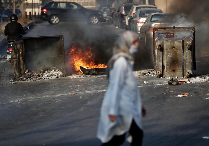 A woman passes in front of burned tires and garbage containers set on fire by anti-government protesters to block roads, during a protest against the economic crisis, in Beirut, Lebanon. AP Photo