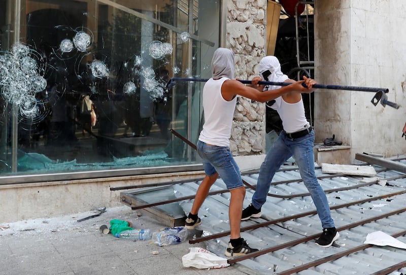 Demonstrators try to break a glass with a metal bar during a protest following Tuesday's blast in Beirut's port area. Reuters