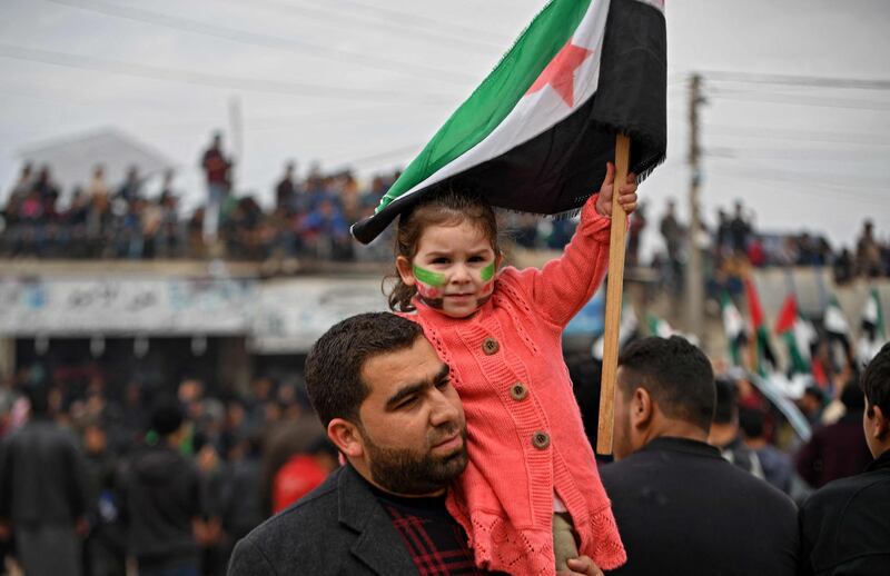 A man holds a girl on his shoulder as she holds a flag of the Syrian opposition during a demonstration in the village of Atme in Syria's rebel-held northwestern province of Idlib close to the border with Turkey. AFP