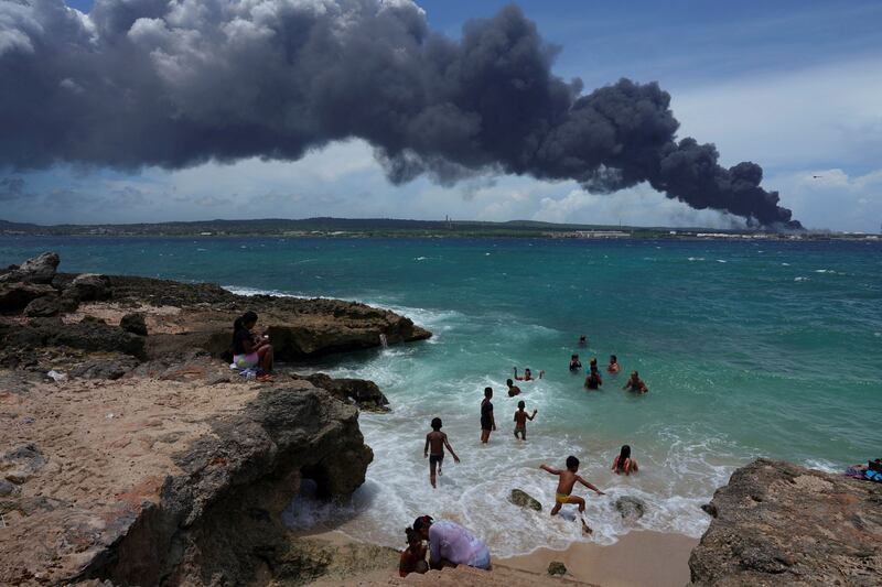 People enjoy the beach near the smoke of a fire after fuel storage tanks exploded in Matanzas, Cuba. Reuters