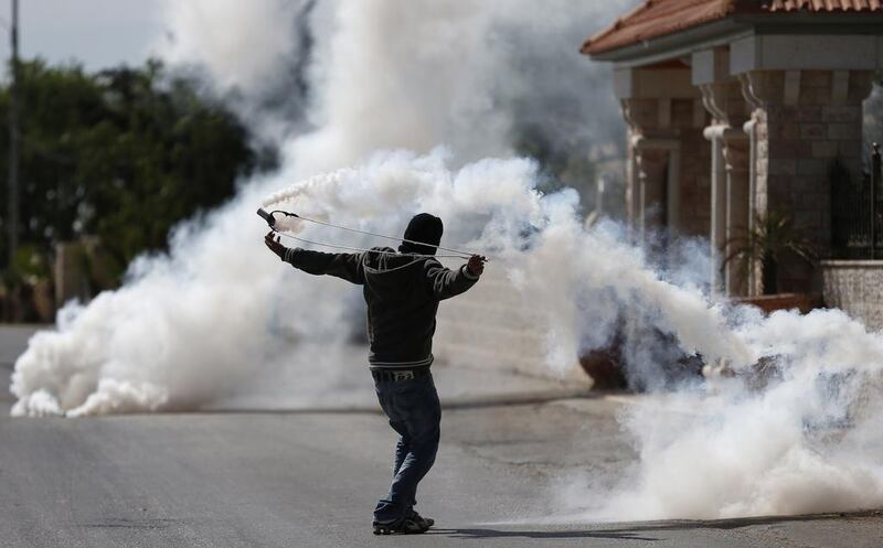 A Palestinian man uses a slingshot to throw back a tear-gas canister towards Israeli soldiers during clashes in the West Bank village of Silwad, north of Ramallah.   Thomas Coex / AFP  