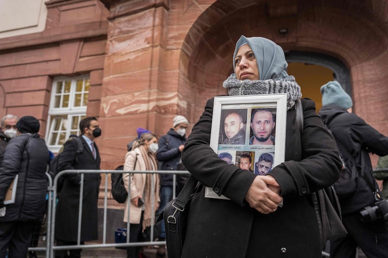 Syrian campaigner Yasmen Almashan holds pictures of victims of the Syrian regime as she and others wait outside the courthouse where former Syrian intelligence officer Anwar Raslan is on trial in Koblenz, western Germany on January 13, 2022 where the verdict is expected on charges for crimes against humanity.  - A historic verdict is expected on January 13, 2022 in the trial of the former colonel of the Syrian intelligence services prosecuted for crimes against humanity - the first procedure in the world linked to the abuses committed by the regime of Bashar al-Assad.  (Photo by Bernd Lauter  /  AFP)