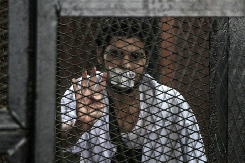 A defendent stands in the accused cells flashing the four finger symbol known as ‘Rabaa’, meaning four in Arabic during the trial of 20 individuals, including five Al-Jazeera journalists, for alleged ties to the blacklisted Muslim Brotherhood and defamation of the country, in the police institute near Cairo’s Turah prison, Cairo, Egypt.  Mohamed El-Shahed / AFP