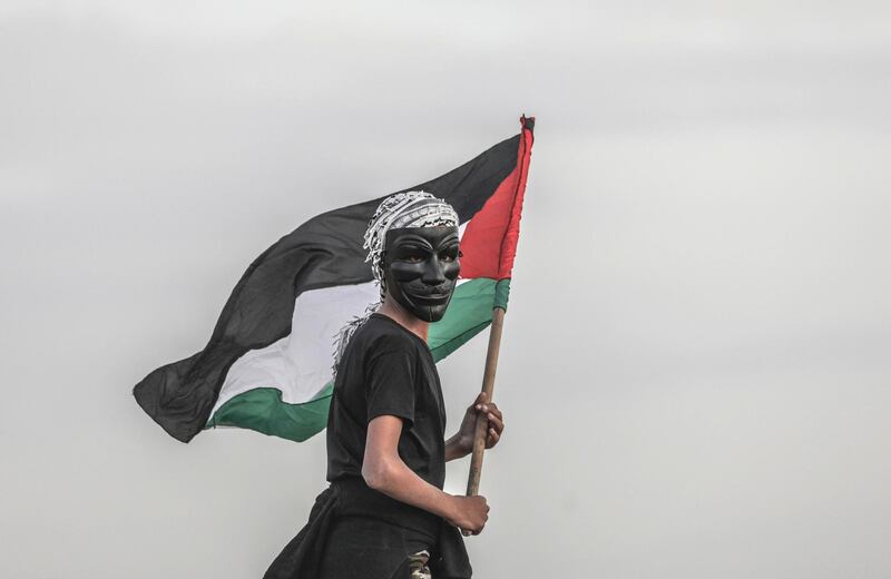 A Palestinian protester wearing a Guy Fawkes mask holds a Palestinian flag during protests.  EPA