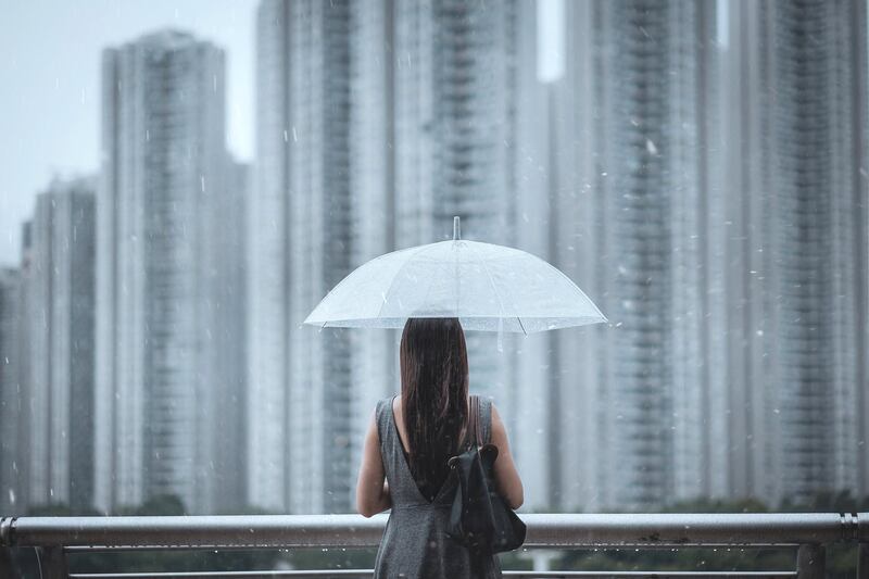 Rear view of young businesswomen with umbrella overlooking the city on a rainy and gloomy day, with blurry highrise residential blocks in the background.