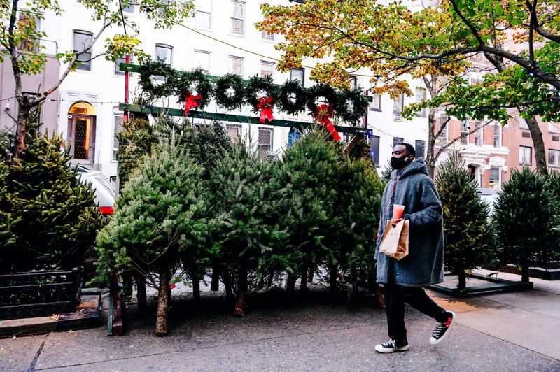 A pedestrian wearing a protective mask passes in front of Christmas trees and wreaths for sale on a sidewalk in New York, U.S. New York City had its credit rating cut by Fitch Ratings because of the impact the coronavirus pandemic is having on the city's economy.  Bloomberg