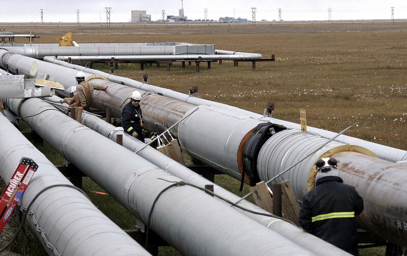 FILE - In this Aug. 18, 2006 file photo BP workers, in the background, remove insulation from an oil transit pipeline at the Prudhoe Bay oil field on Alaska's North Slope. BP, a major player on Alaska's North Slope for decades, is selling all of its assets in the state, the company announced Tuesday, Aug. 27, 2019. Hilcorp Alaska is purchasing BP interests in both the Prudhoe Bay oil field and the trans-Alaska pipeline for $5.6 billion, BP announced in a release. (AP Photo/Al Grillo)