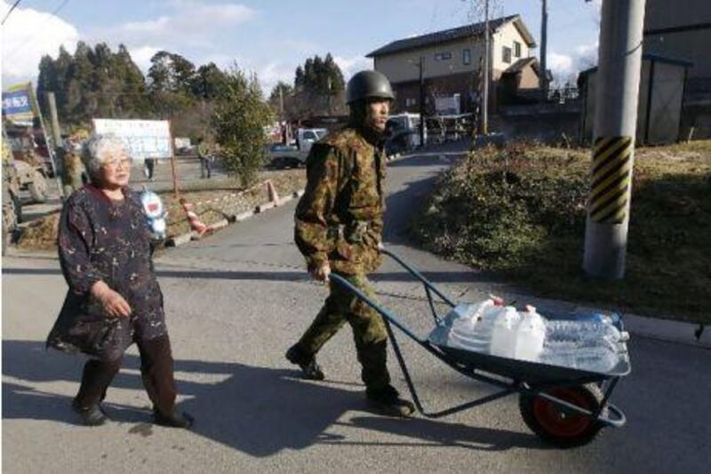 An elderly woman is helped by a Japanese soldier to carry the plastic bottles and tanks she filled with tap water from a water truck in the tsunami-hit coastal city of Kesennuma, northeastern Japan.