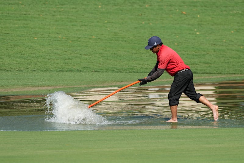 An employee of the golf course tries to push rain water off a fairway during the round two. AP