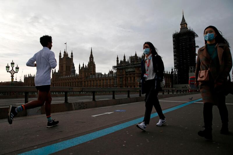 Pedestrians wearing a face masks or coverings due to the COVID-19 pandemic, walk across Westminster Bridge, near the Houses of Parliament in central London on November 16, 2020.  / AFP / POOL / Hollie Adams
