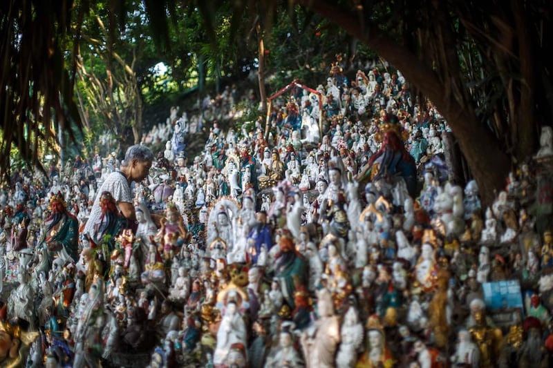 An elderly woman walks past unwanted statues of deities, gathered and repaired after their owners discarded them, on a rocky slope running down to the sea in Hong Kong. Anthony Wallace / AFP

