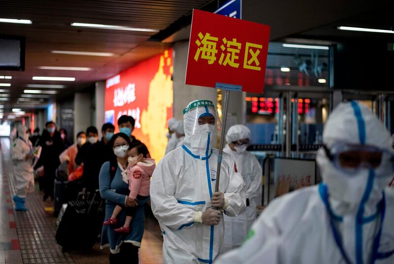 Transport personnel wearing hazmat suits guide travellers arriving from Wuhan to buses, which will take them to their quarantine locations, at Beijing West Railway Station.   AFP