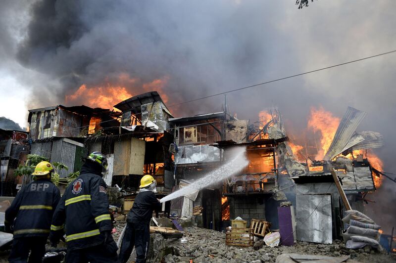 Firefighters extinguish flames as a fire engulfs an informal settlers area beside a river in Manila on August 11, 2017.
Fires are common hazards in the sprawling capital, where millions live in hovels made of scrap wood and cardboard and fire safety regulations are rarely imposed. / AFP PHOTO / NOEL CELIS